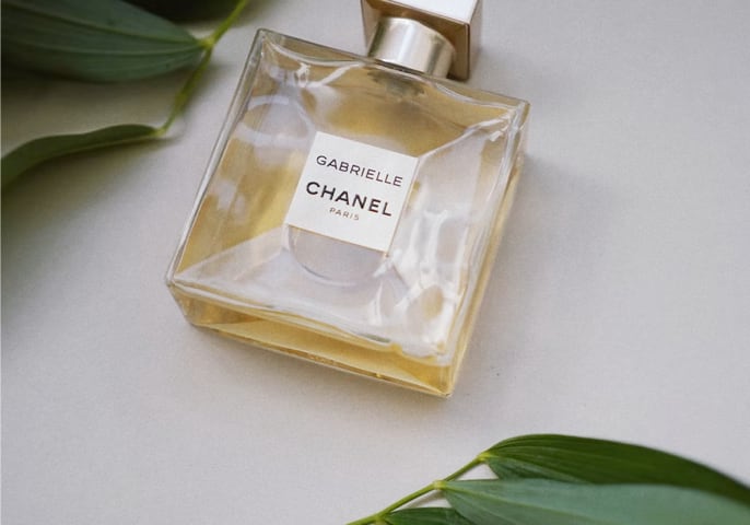 Bottle of Gabrielle Essence Eau De Parfum laying flat on a table surrounded by leaves